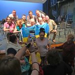 Conductor Theodore Kuchar, center, with members of the Lvivi National Philharmonic Orchestra of Ukraine, posing with a Ukrainian flag after a two-hour rehearsal at the Flagler Auditorium Thursday evening. The audience was largely made up of students and families of the Flagler Youth Orchestra community. (© FlaglerLive)